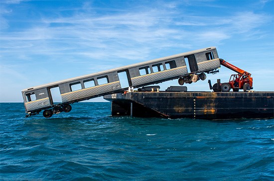 A retired MARTA railcar is carefully tipped from a barge into the Atlantic Ocean
